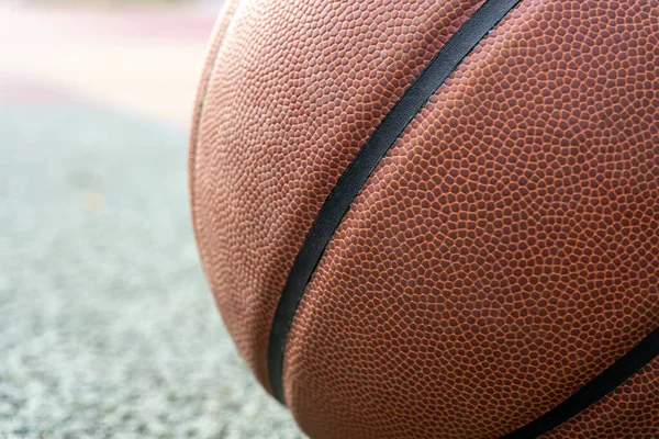 Orange basketball ball on the ground. Close-up ball on the red court. Basketball on the street or indoor court. Sports gear without people. Minimalism. Template, sport background