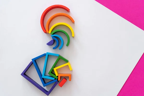 Abstract rainbow background. Wooden kids toys on white magenta paper. Educational toys blocks, rainbow. Toys for kindergarten, preschool or daycare. Copy space for text. Top view