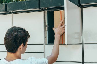 Man opening a door of post office box on the city street and receive a parcel. Man carrying box from post office delivery