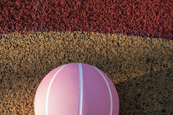 Pink basketball ball on the ground. Close-up ball on the red court. Basketball on the street or indoor court. Sports gear without people. Minimalism. Template, sport background