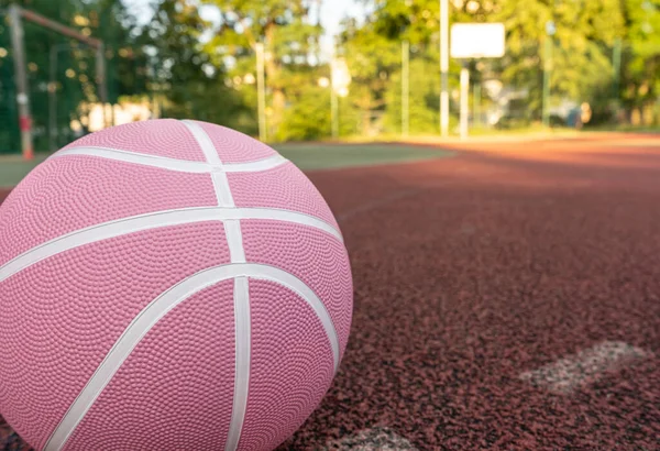 Pink basketball ball on the ground. Close-up ball on the red court. Basketball on the street or indoor court. Sports gear without people. Minimalism. Template, sport background