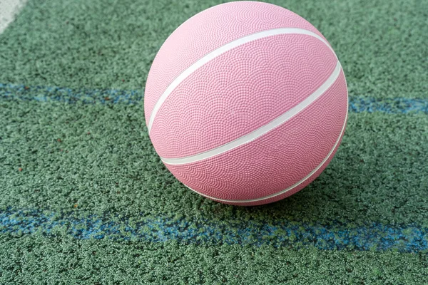 Pink basketball ball on the ground. Close-up ball on the red court. Basketball on the street or indoor court. Sports gear without people. Minimalism. Template, sport background