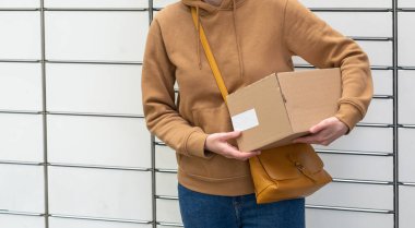 Otomatik paket makinesinin yanındaki kutulu kadın. Elinde karton bir kutu tutan kişi. Posta ve posta servisi, online alışveriş, e-ticaret konsepti.