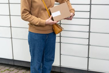 Otomatik paket makinesinin yanındaki kutulu kadın. Elinde karton bir kutu tutan kişi. Posta ve posta servisi, online alışveriş, e-ticaret konsepti.