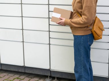 Otomatik paket makinesinin yanındaki kutulu kadın. Elinde karton bir kutu tutan kişi. Posta ve posta servisi, online alışveriş, e-ticaret konsepti.