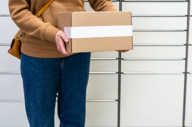 Otomatik paket makinesinin yanındaki kutulu kadın. Elinde karton bir kutu tutan kişi. Posta ve posta servisi, online alışveriş, e-ticaret konsepti.