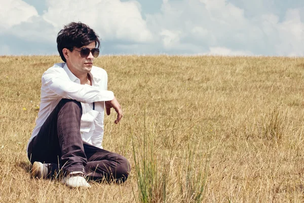 Genç adam çayır üzerinde siting — Stok fotoğraf