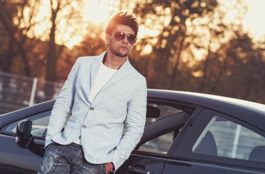 trendy yakışıklı genç adamın arabasına yaslanarak
