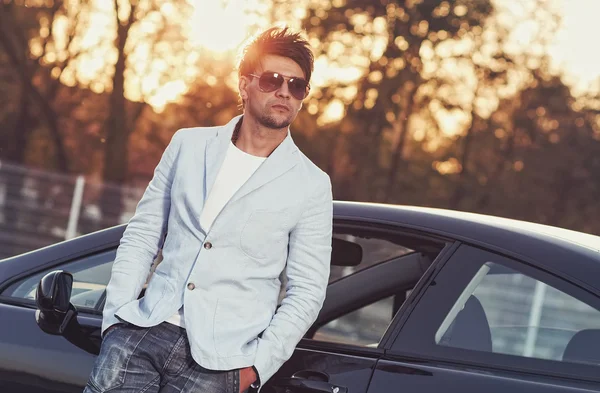 Модный красивый молодой человек, опирающийся на свою машину — стоковое фото