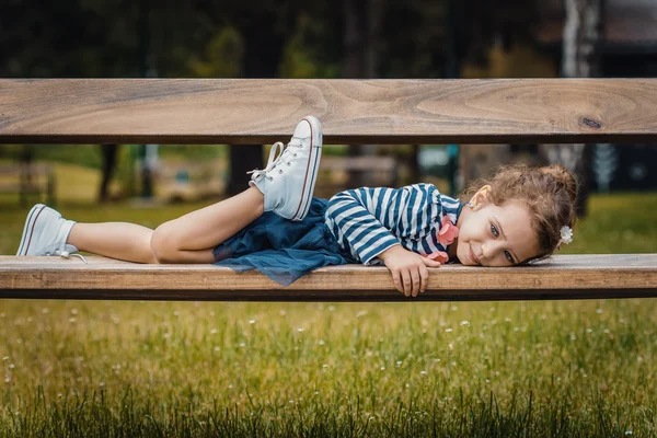 Un placer niña acostada en un banco en un parque — Foto de Stock