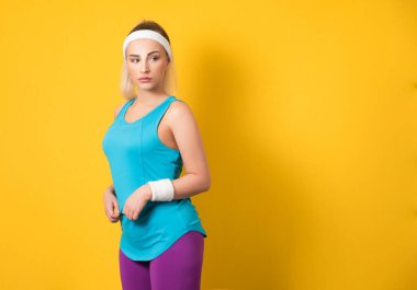 Genç kadın poz veriyor ve yana bakıyor, sarı arka planda izole edilmiş. Sporcu kadın yarı uzunluğunda egzersiz için hazır. Atletik kadın. 80 'lerin stili. Stüdyo çekimi