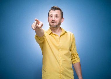 Şakacı adam sana gülüyor ve mavi arka planda kamerayı işaret ediyor, sarı gömlekli. Gülen bir adam. Şaka ve şaka. Stüdyo çekimi