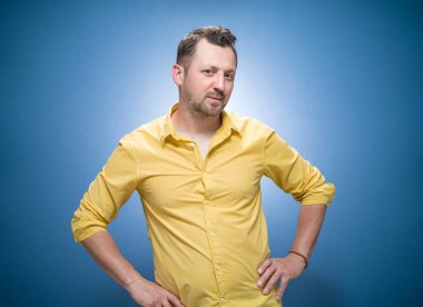 Genç adamın düşündüğü eğlenceli düşünceler. Mavi arka planda ilham verici bir adamın portresi, sarı gömlekli. Stüdyo çekimi