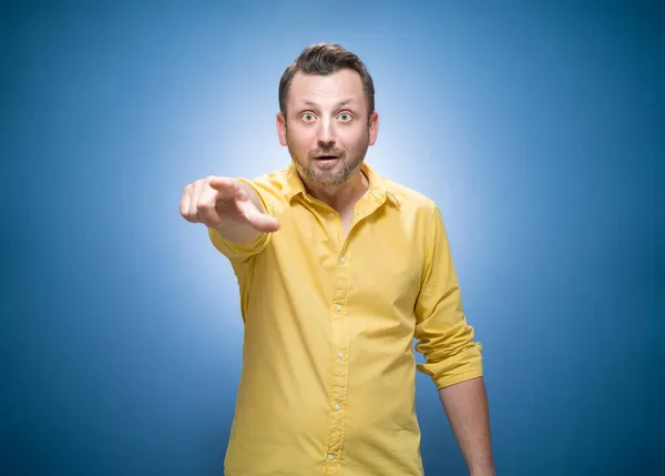 面白い怖い男を指しているか 青い背景の上に何かに指で示す 黄色のシャツのドレス スタジオショット — ストック写真