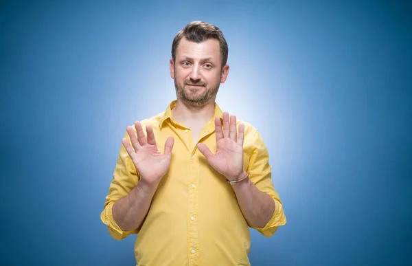 青い背景の上に何かを拒否または拒否し 黄色のシャツに身を包んだ 手の手のひらで停止記号をジェスチャー若い男 スタジオショット — ストック写真