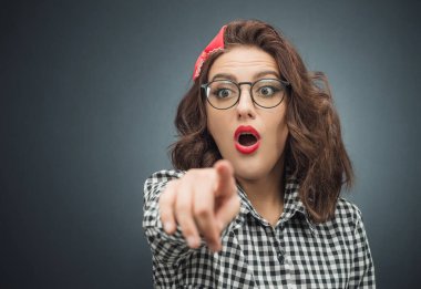 Komik, korkmuş bir kadın koyu gri arka planda bir şeyi işaret ediyor ya da gösteriyor. Stüdyo çekimi