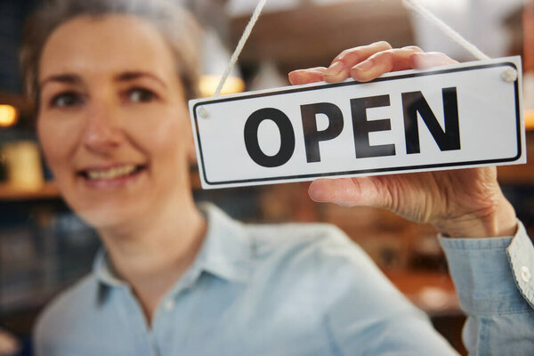 Female Owner Of Small Business Turning Round Open Sign On Door