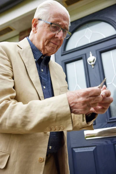 Confused Senior Man With Early Stage Dementia Trying To Find Correct Door Key Outside House