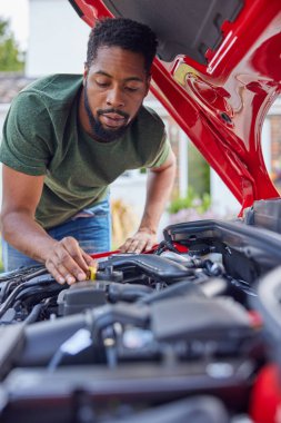 Motor yağı seviyesini kontrol eden kaputun altında çalışan bir adam var.