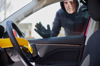 Male Thief Looking Through Window At Manual Steering Wheel Lock In Car