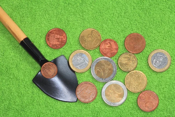 Coins, shovel on a green background. — Stock Photo, Image