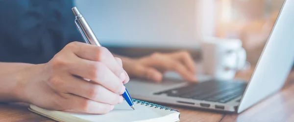 İş kadını bir not defterine kalemle el yazısı ve ofisteki dizüstü bilgisayarı kullan. Web afişi için..