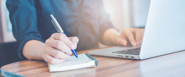 İş kadını bir not defterine kalemle el yazısı ve ofisteki dizüstü bilgisayarı kullan. Web afişi için..