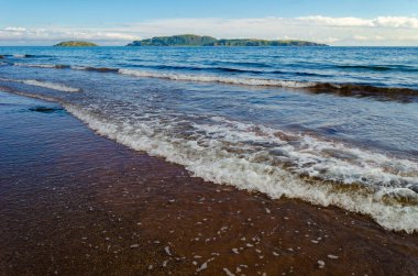 Uzakta Sanda Adası ve Koyun Adası ile Kintyre Mull yakınlarında, Southend 'deki İskoç sahillerinde dalgalar kopuyor.