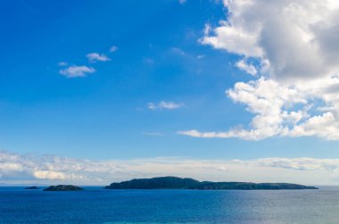 Sanda Adası ve Koyun Adası, mavi deniz mavi gökyüzü ve Kintyre İskoçya Mull yakınlarındaki beyaz bulutlarla dolu bir yaz günü.