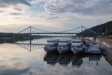 KYIV, UKRAINE - 21 Temmuz 2019: Dnipro nehri kıyısındaki yaya köprüsüne yakın tekneler.