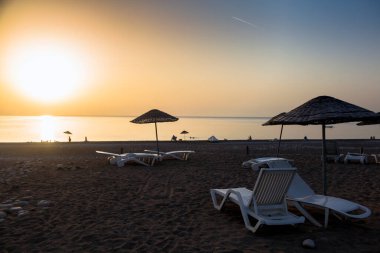 Akdeniz kıyısında kum ve küçük çakıl taşlarının karışımından oluşan plajdaki beyaz turist güneşlikleri