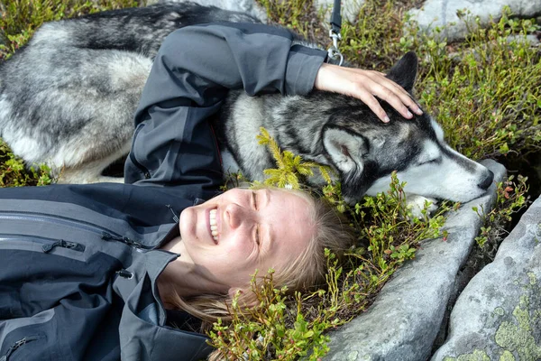 Funny portrait of a beautiful Siberian Husky dog sleeping and a tourist girl smiling in the green grass background, outdoor hiking scenario