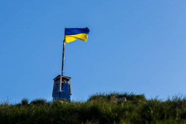 Ukrayna bayrağı ufuktan yükselen bir tepede mavi gökyüzünün arka planına karşı