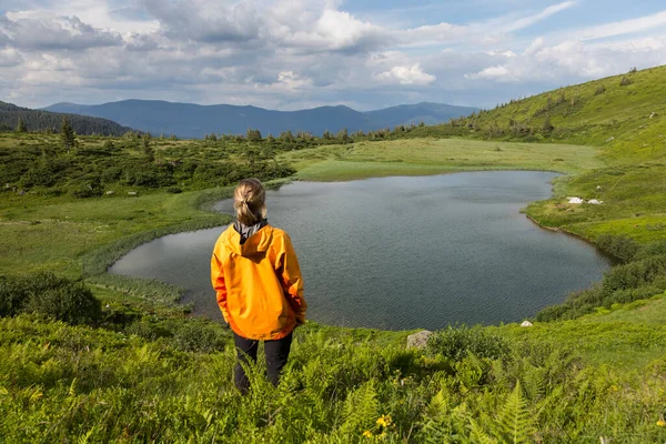 A hiking girl looks at the bowl of a mountain lake surrounded by forests and peaks, Carpathians
