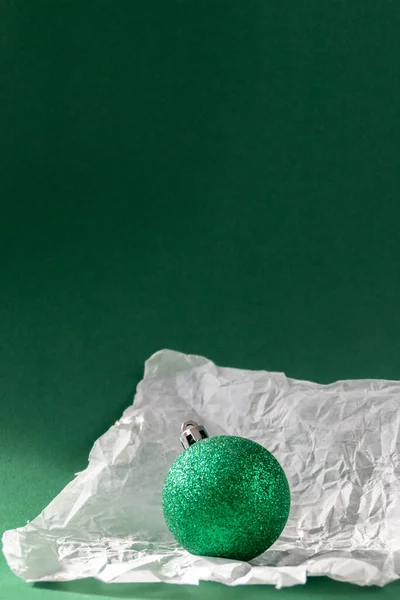 Green Christmas ball in torn paper against emerald green background