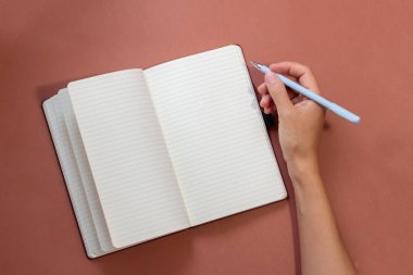 Kahverengi arkaplan üzerinde kalem ve defter ile el