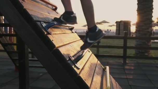 Boy climbs up the ladder in playground. Going up in sunset in slowmotion closeup — Stock Video