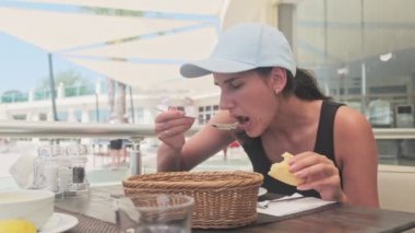 Şehirdeki restoranda mısır çorbası içen mavi şapkalı genç bir kadın.