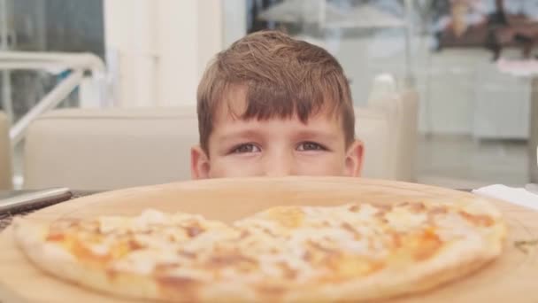 小孩吃比萨 饥饿的小男孩吃着盘子里美味的意大利比萨 不健康的营养快餐 小孩吃午饭的肖像 面对年轻男孩的衣服 — 图库视频影像