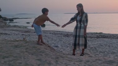 Sevecen, mutlu bir anne yazın deniz kıyısında yürürken sevgili oğluna sarılır. Küçük çocuk yazın annesine dışarıda sarılıyor. Mutlu aile, anne, oğul, çocuk şefkatle kucaklaşması.