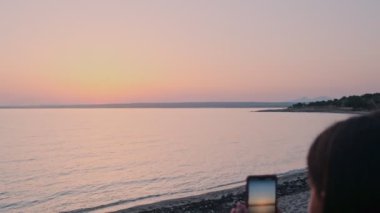 Güzel bir kız telefonda güneşin doğuşunu fotoğraflıyor. Kız gün doğumunda sevinir. Dinlen, turizm.
