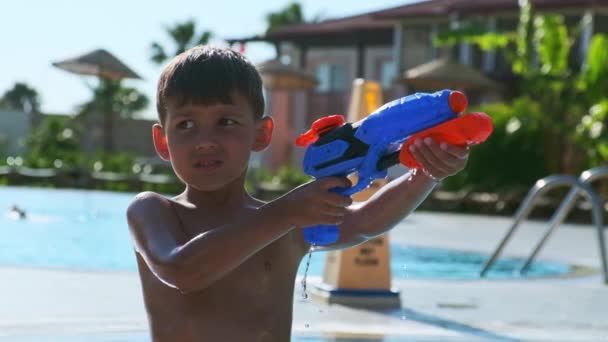 一名小男孩在热带旅游胜地的公共游泳池里向玩具枪射击的特写镜头 — 图库视频影像