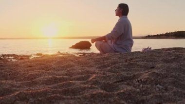 Deniz kenarında dinlenme egzersizi yapan genç bir kadın. Denizin üzerinde altın gün batımı yoga yapıyor. Kumsalda gün batımı güneşin önünde yavaş yavaş meditasyon yapıyor.