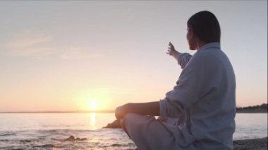 Deniz kenarında dinlenme egzersizi yapan genç bir kadın. Denizin üzerinde altın gün batımı yoga yapıyor. Kumsalda gün batımı güneşin önünde yavaş yavaş meditasyon yapıyor.