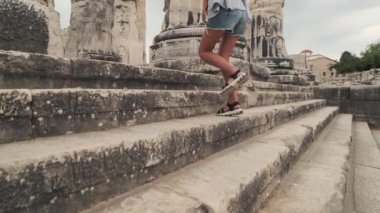 Sandaletli bir kadın, güneşli bir günde antik şehrin merdivenlerinden çıkar. Yavaş çekimde, turist zirveye tırmanır. Dinlen, seyahat et, tırman. Güzel görüntüler. döşeme