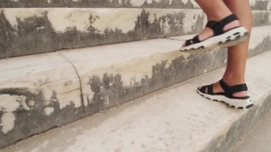 Sandaletli bir kadın, güneşli bir günde antik şehrin merdivenlerinden çıkar. Yavaş çekimde, turist zirveye tırmanır. Dinlen, seyahat et, tırman. Güzel görüntüler. döşeme