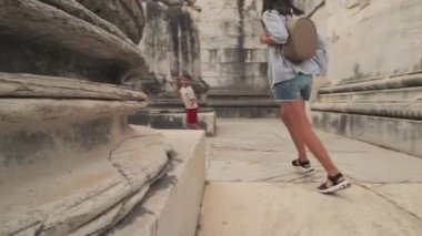 Young mom and her son have fun when runing between columns in the ancient city summer at sunset. Lifestyle. Outdoors. Slowmotion