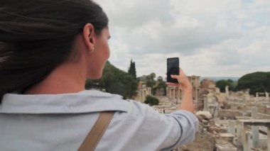 Millennial hipster girl tourist in casual outfit photographing buildings and architecture in ancient city using camera and application on modern cellular phone, slow motion effect. Female wanderlust