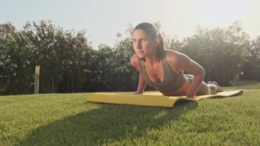 Spor kıyafetli kadın dışarıda yoga pozu veriyor. Parkta esneme hareketleri yapan atletik kız. Spor salonundaki kadın yeşil çimenler üzerinde yoga egzersizleri yapıyor. Açık havada spor yapan bir kız. Yavaş çekim