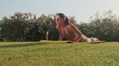 Spor kıyafetli kadın dışarıda yoga pozu veriyor. Parkta esneme hareketleri yapan atletik kız. Spor salonundaki kadın yeşil çimenler üzerinde yoga egzersizleri yapıyor. Açık havada spor yapan bir kız. Yavaş çekim